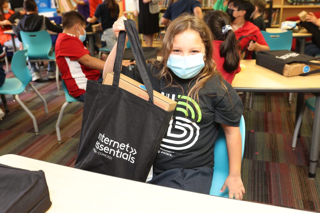 A young student holds up an Internet Essentials bag and laptop.